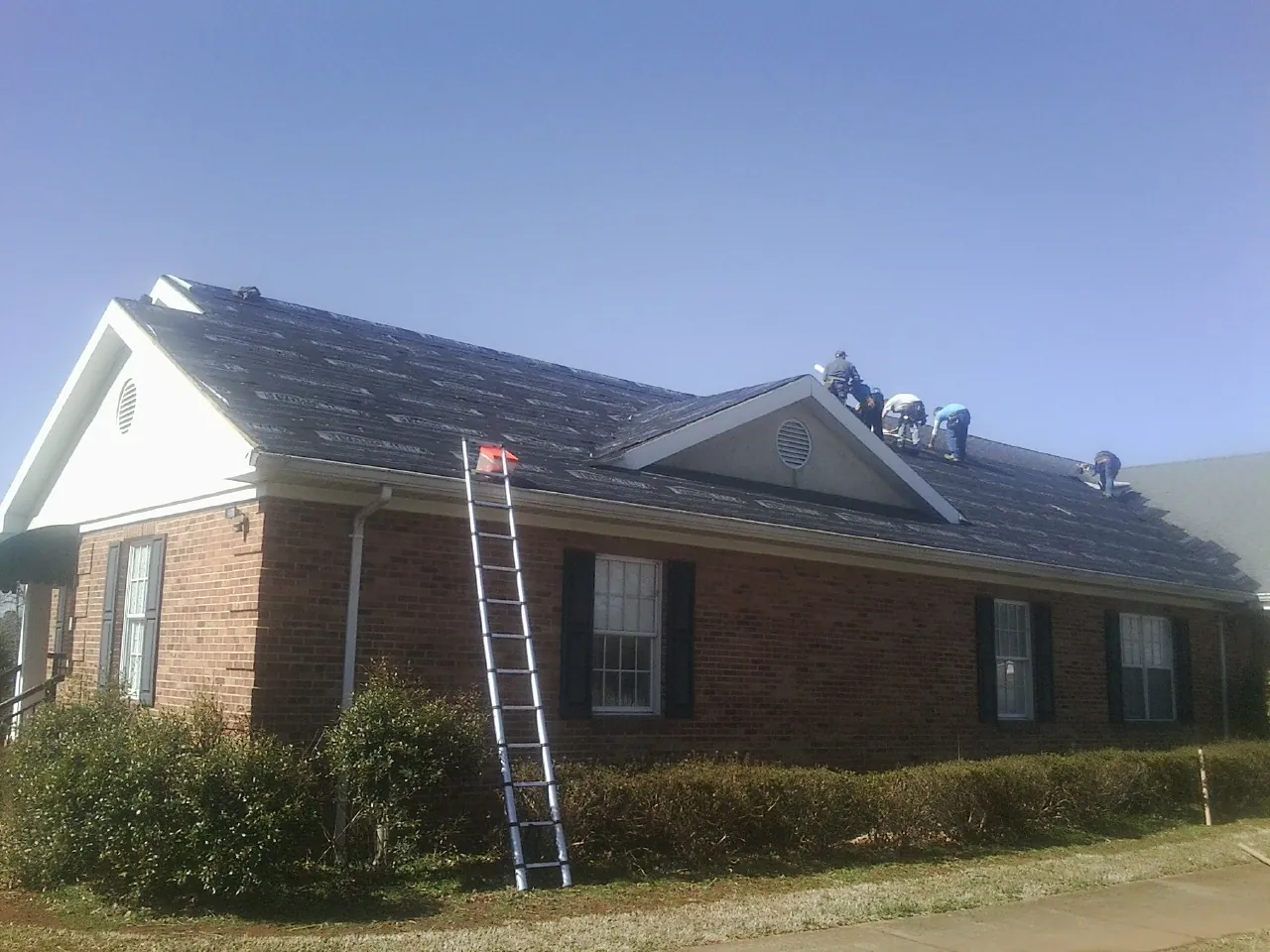 Crew tearing shingles off a brick ranch roof with a ladder set — Metal Roof Repair work by our crew in Martell