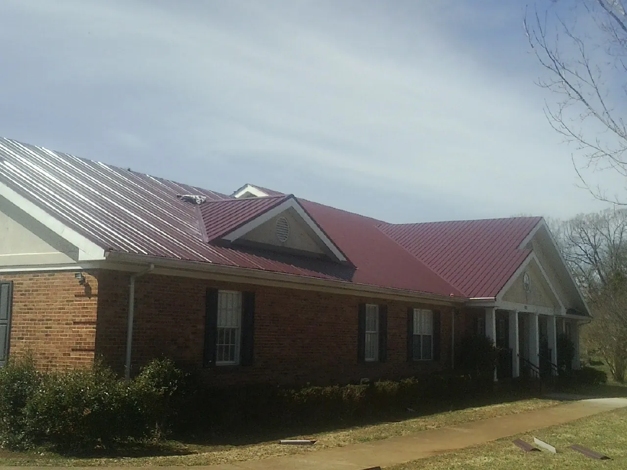 Red metal roof with gabled entries on a long brick building, from a Hail Damage Roof Repair job in Martell