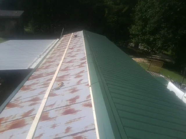 Old rusted panels beside newly installed green metal roofing — Wind Damage Roof Repair by Roofing Brothers in Martell