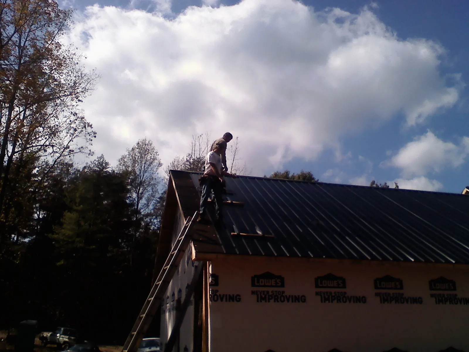 Roofer fastening dark metal panels high against a cloudy sky, from a Roof Inspection job in Martell