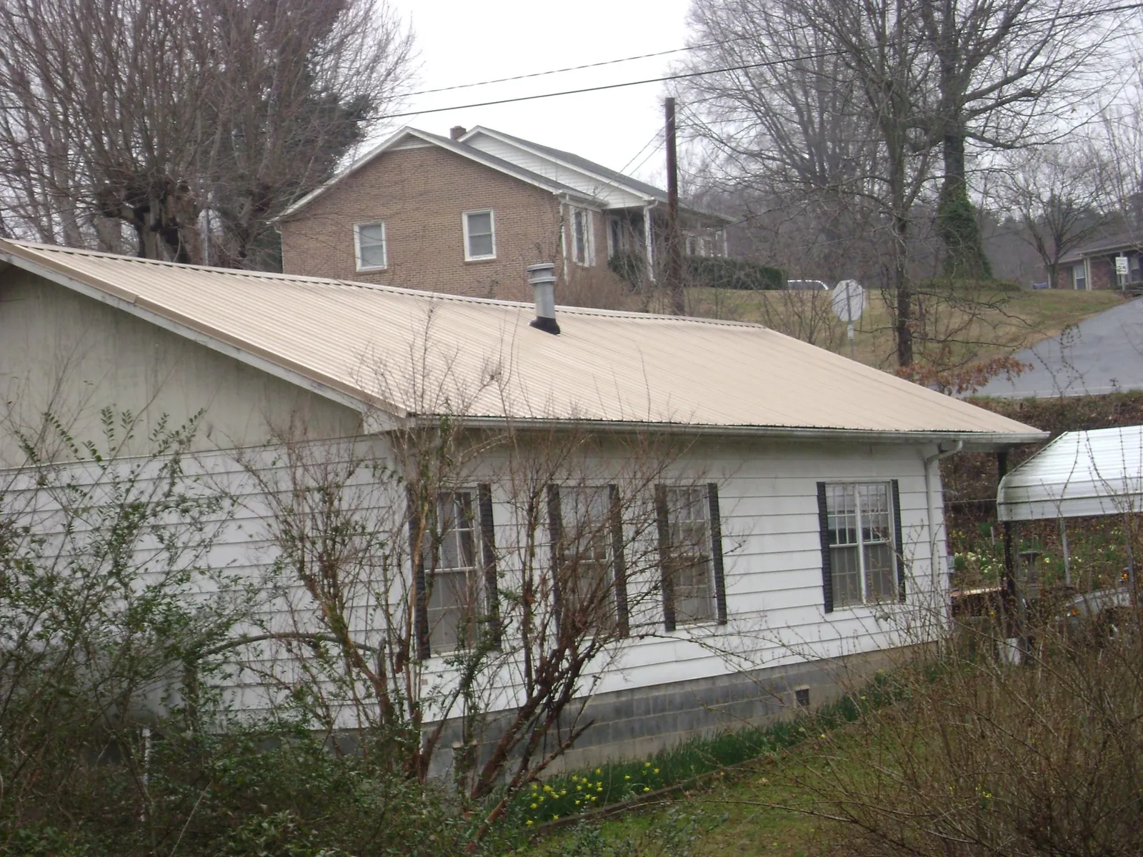 Tan metal roof on a white sided house set into a hillside — Commercial Roofing by Roofing Brothers in Martell