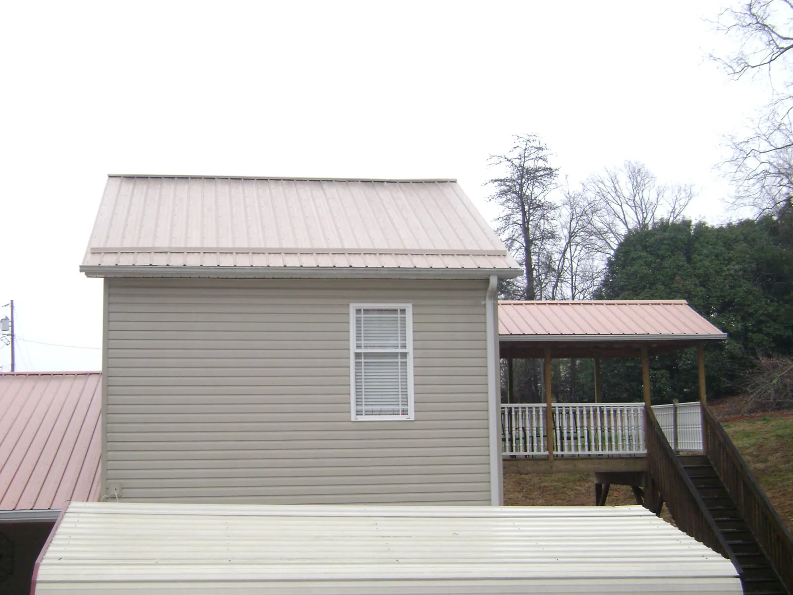 Tan metal roofs on a two story addition and attached porch, from a Roof Replacement job in Martell